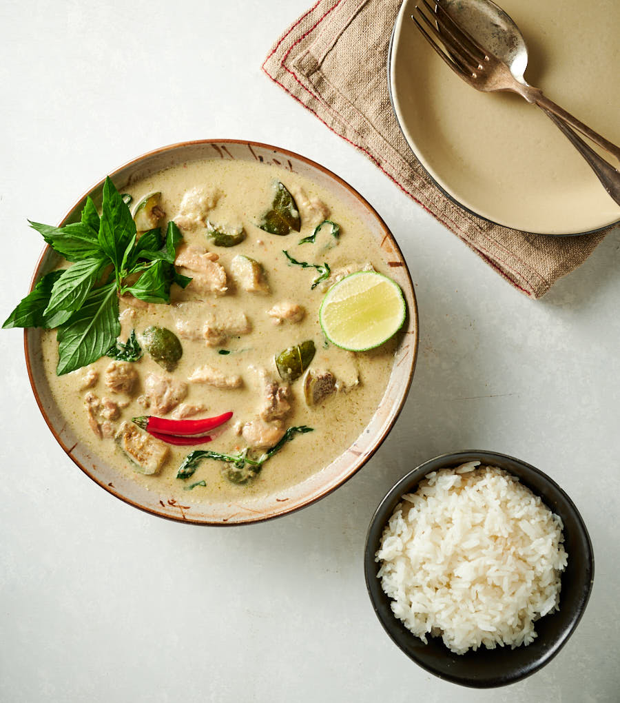 Thai green curry in a bowl, rice and serving dishes from above.