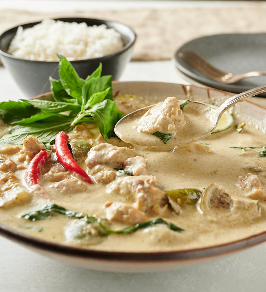 Spoonful of Thai green curry above a bowl of curry.