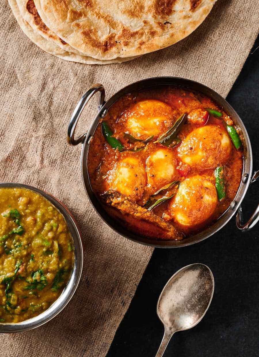 Egg curry, dal and parathas on a burlap background from above.