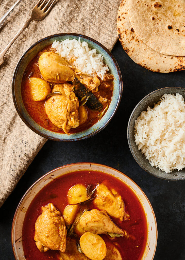 Scène de table avec kari ayam dans un bol avec du riz à côté d'un plateau de service rempli de curry.