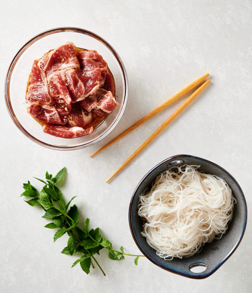 pork in marinade and bowl of cooked rice noodles