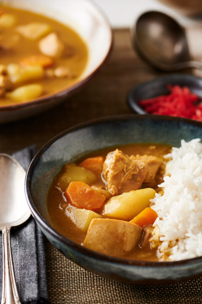 Bowl of Japanese curry and rice with larger bowl of curry in the background from the front.