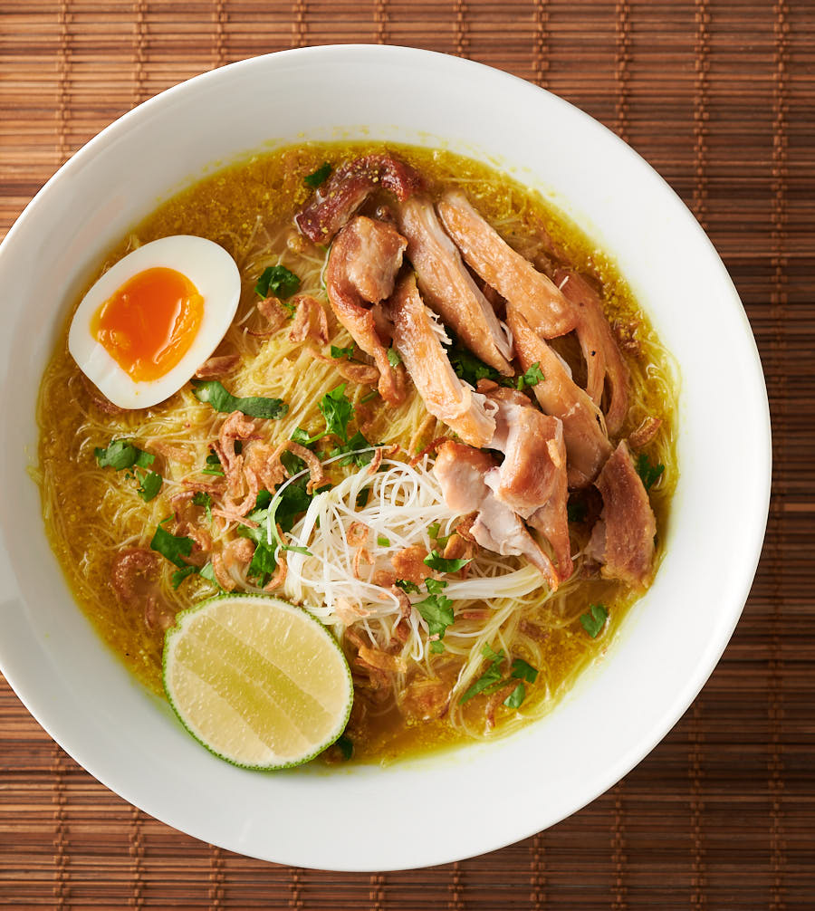Bowl of soto ayam on bamboo background from above.