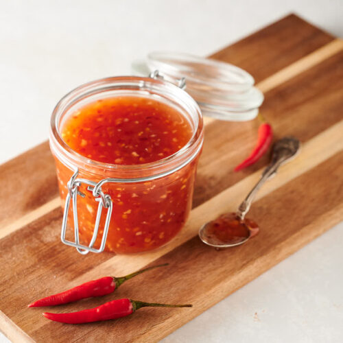 Spoonful of Thai sweet chili sauce next to a mason jar full on a cutting board.