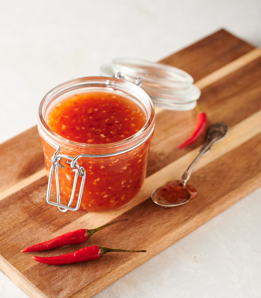 Spoonful of Thai sweet chili sauce next to a mason jar full on a cutting board.