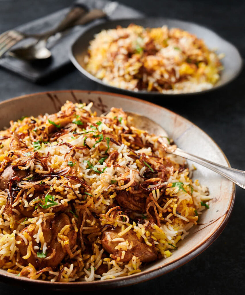 Chicken biryani in a bowl with serving spoon from the front.