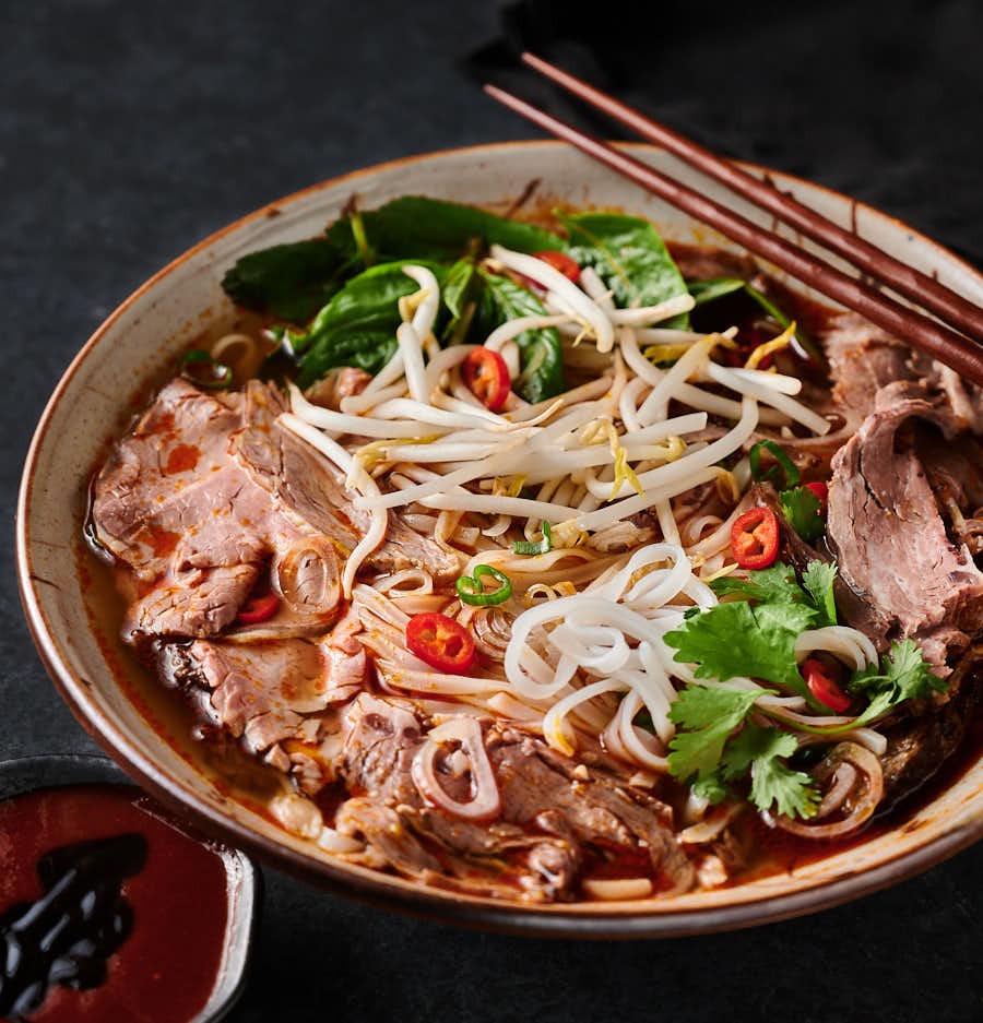 Spicy beef noodle soup in a bowl with chopsticks from the front.