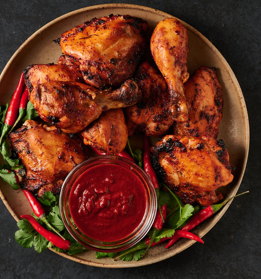 Tandoori chicken and a small bowl of tandoori paste on a plate from above.