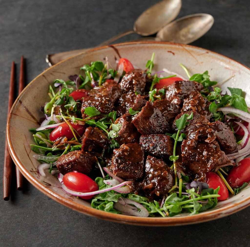 Bowl of shaking beef salad in a low round bowl from the front.