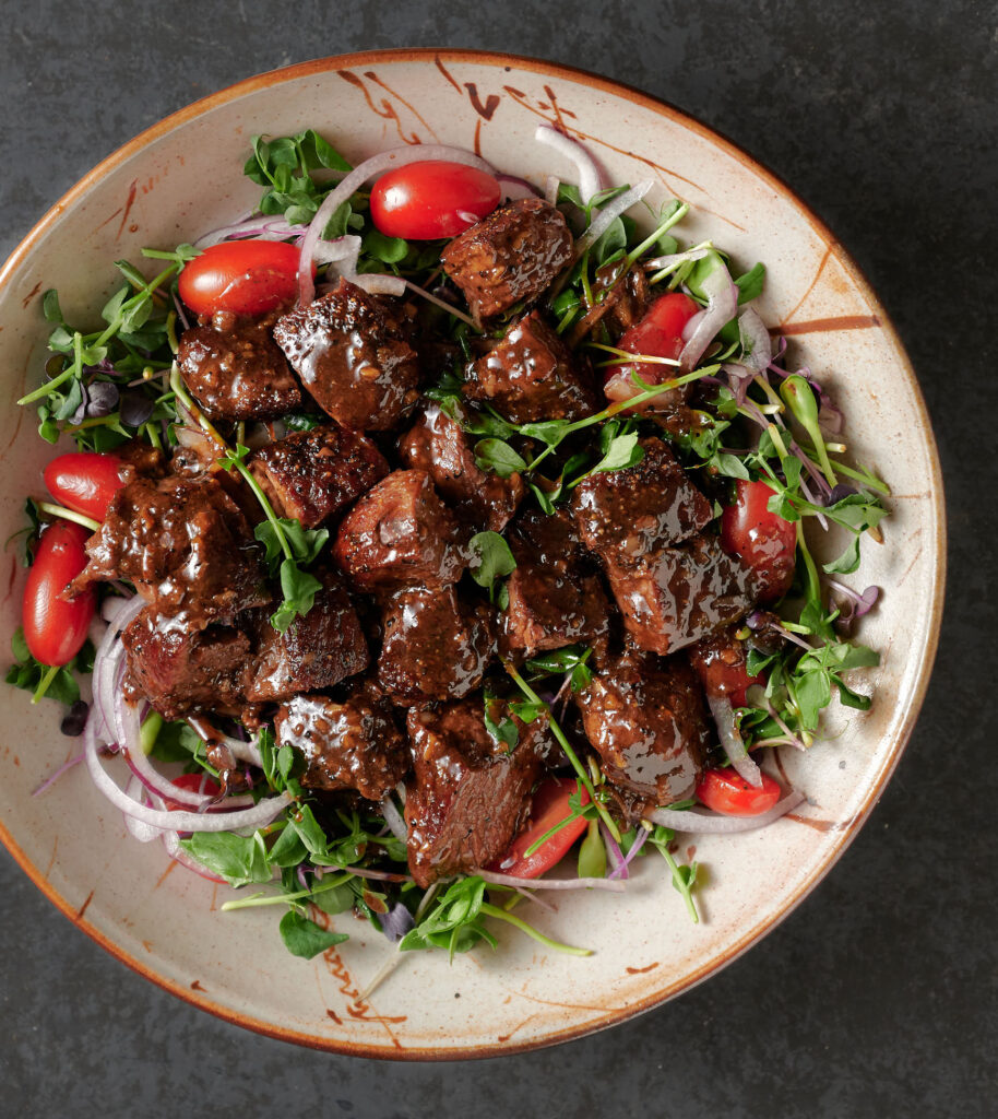 Bowl of shaking beef on a bed of micro-greens from above.