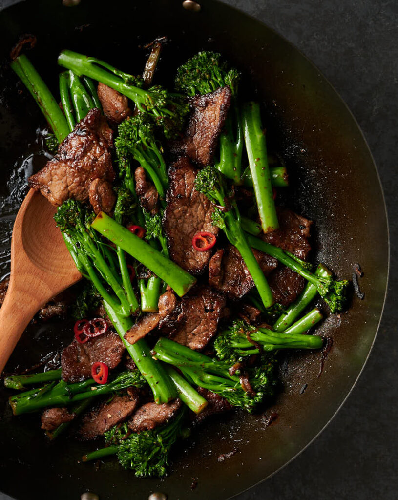 Wok full of Thai beef and broccoli with wooden spoon from above.