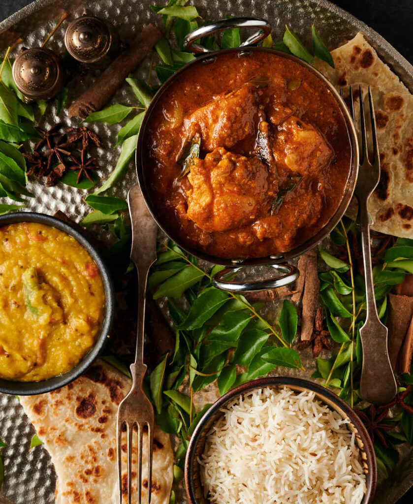 Chettinad chicken curry, dal, rice and parathas on a platter from above.