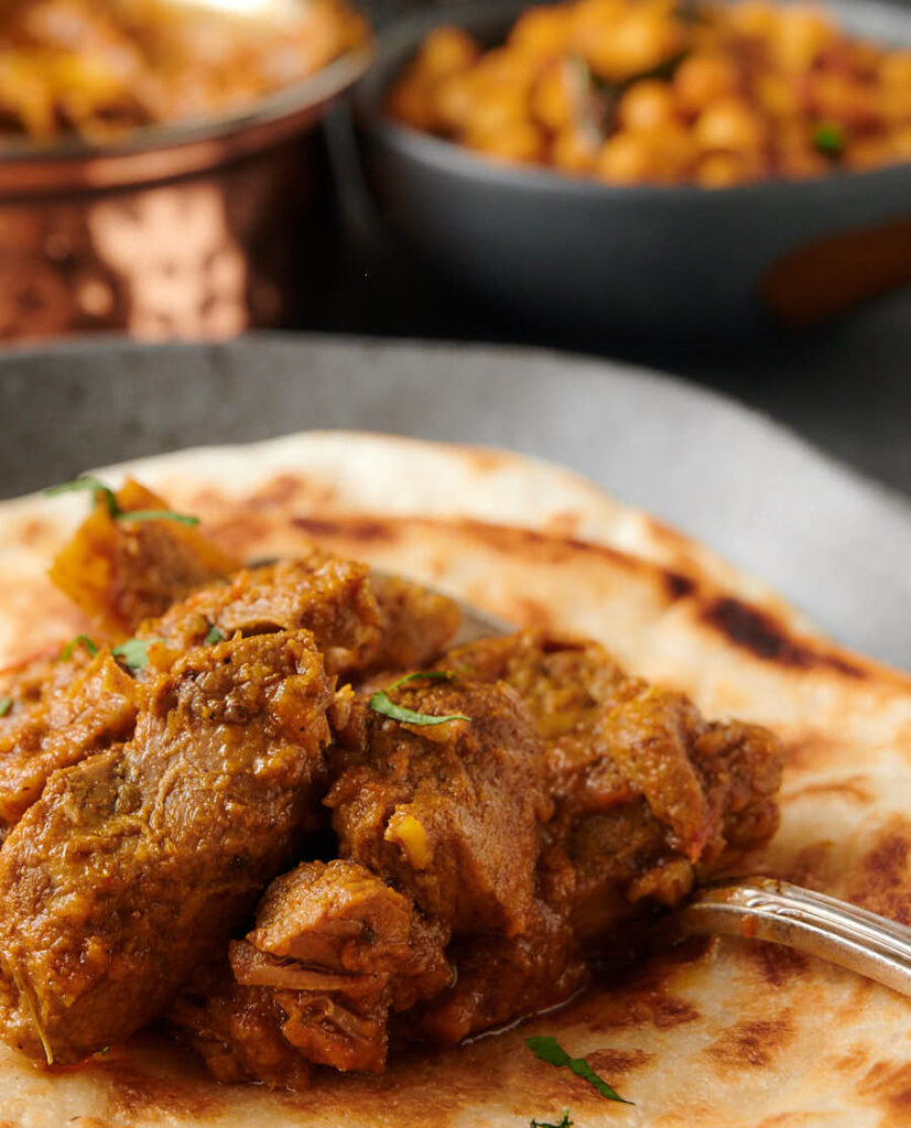 Closeup of a big spoonful of lamb madras on a paratha.