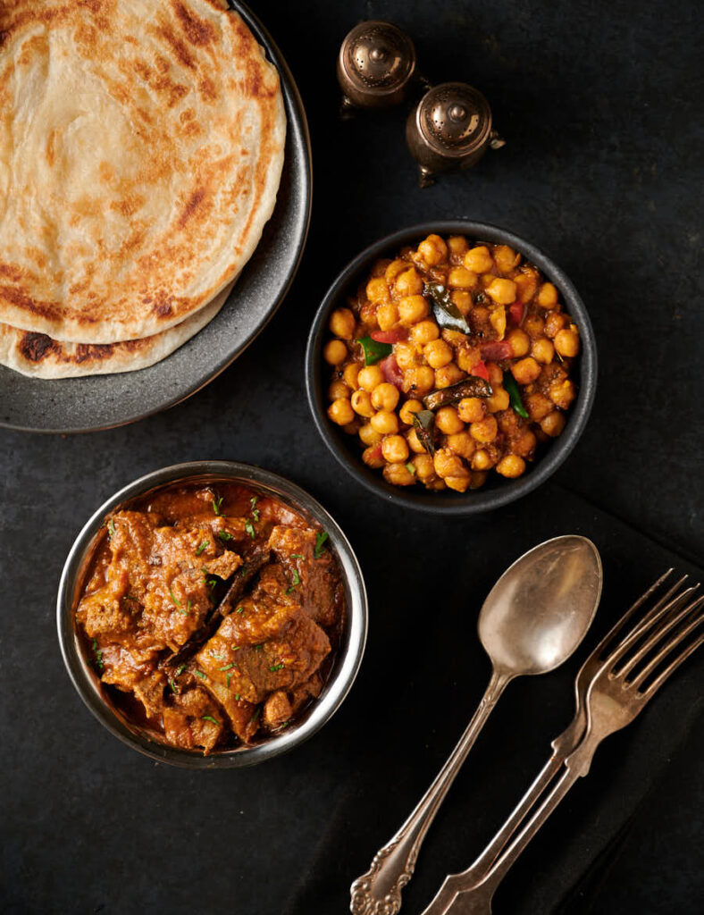 Table scene with Indian hotel style lamb madras, channa masala and parathas from above