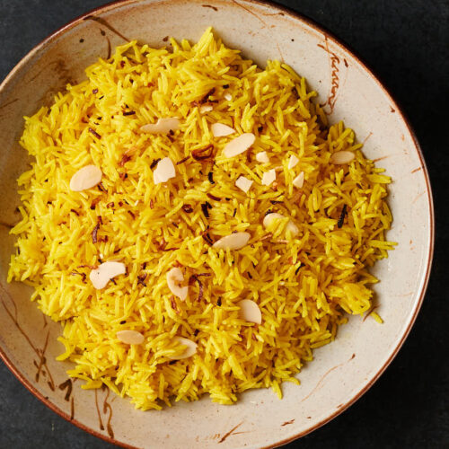Bowl of turmeric coloured Indian restaurant style rice pilau from above.