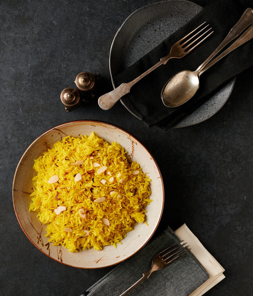 Top down table scene - rice pilau, plate, seasoning shakers and antique cutlery from above.