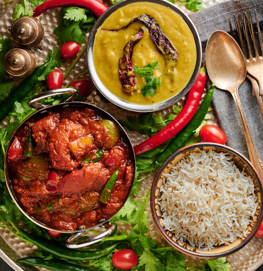Table scene with chicken tikka jalfrezi, dal and rice from above.