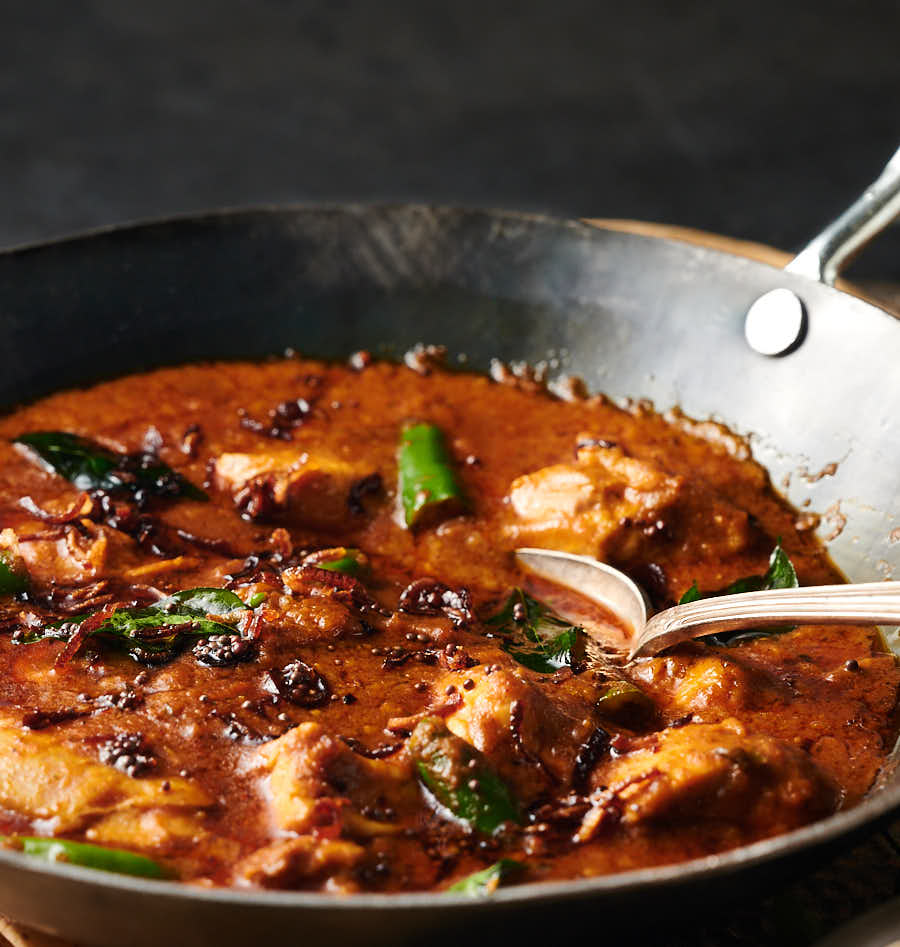 Closeup of Kerala chicken curry garnished with fried curry leaves.