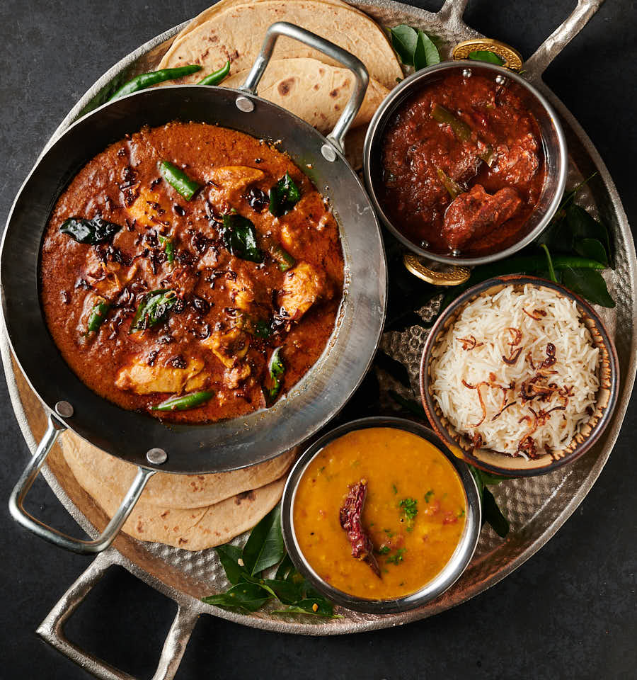 Table scene of hotel style Kerala chicken curry with rice, dal and chapatis.