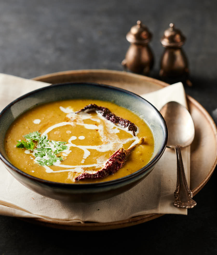 Bowl of mulligatawny soup garnished with drizzled cream, cilatntro and whole kashmiri chilies from the front.