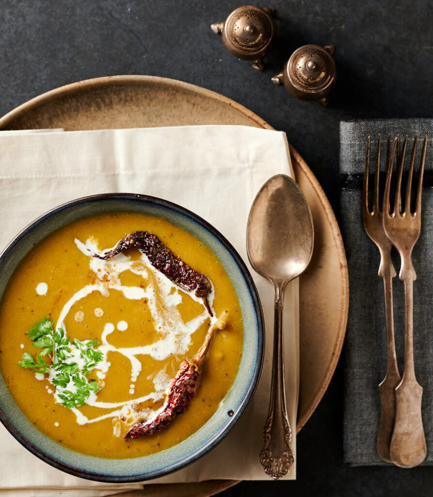 Escena de mesa con un tazón de sopa mulligatawny en una servilleta blanca en un plato con cuchara de plata vieja.