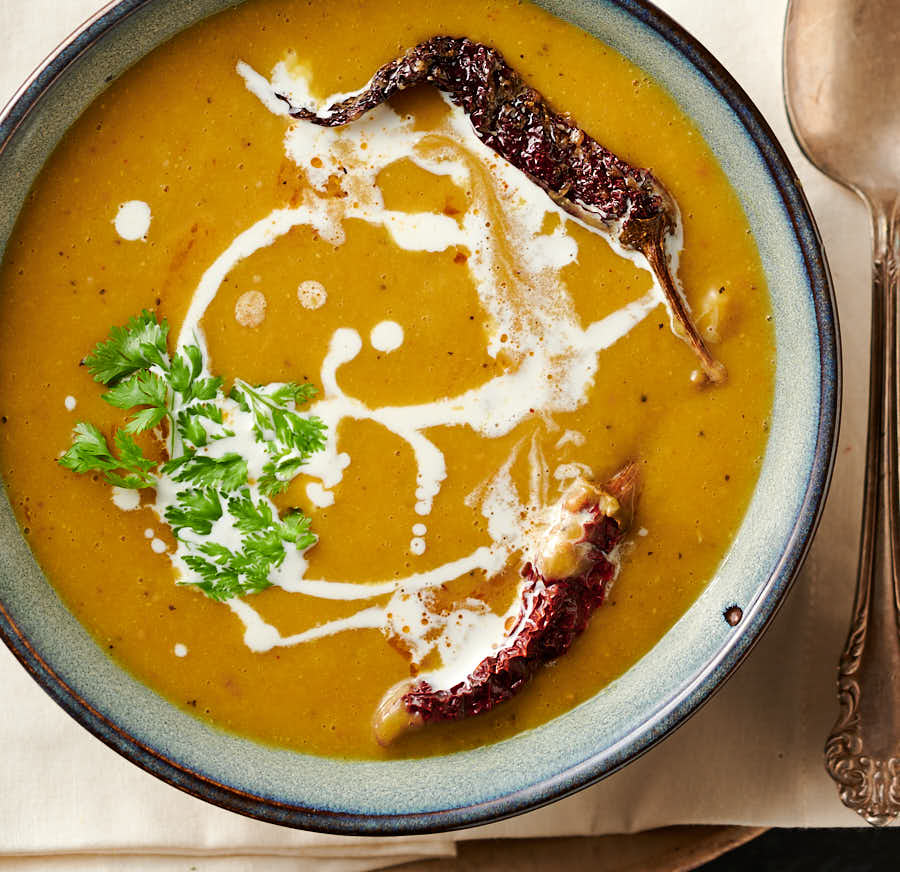 Ciotola di zuppa mulligatawny guarnita con peperoncini del kashmir, crema e coriandolo dall'alto.