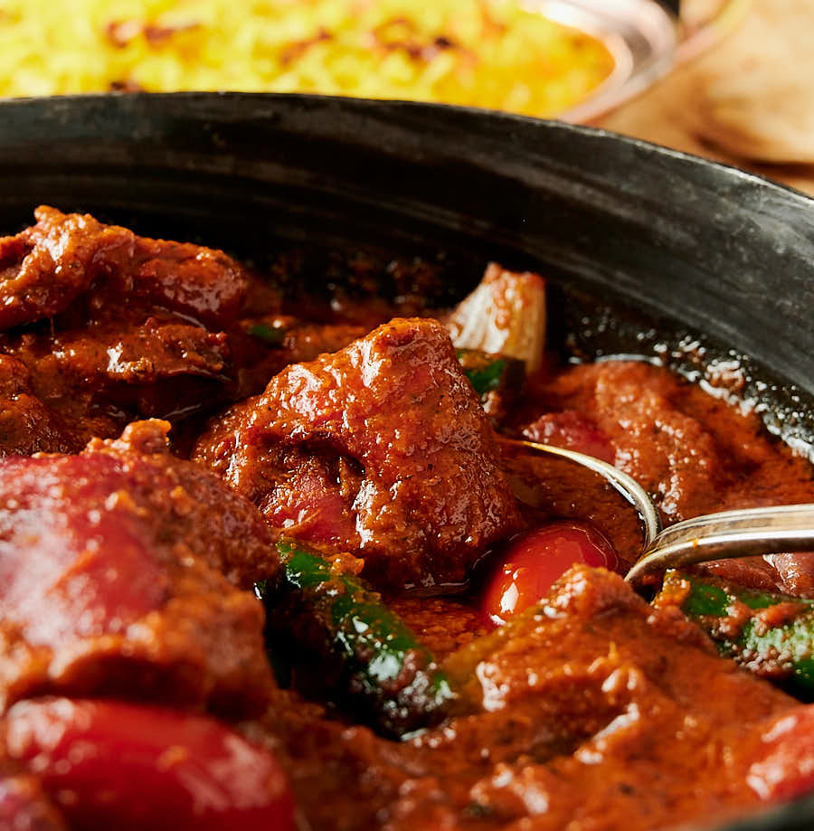 Closeup of spoon in a bowl of chicken tikka jalfrezi from the front