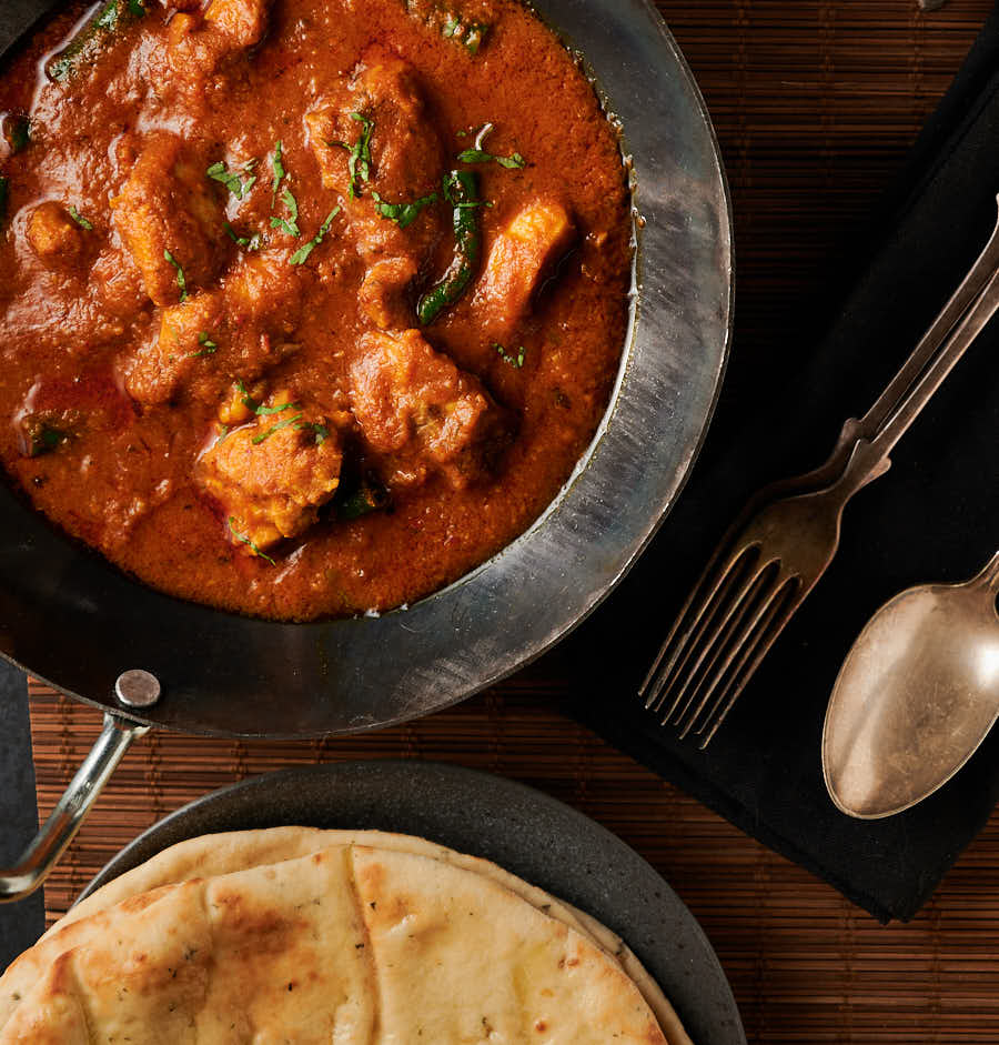 Achari chicken curry in a kadai with naan from above.