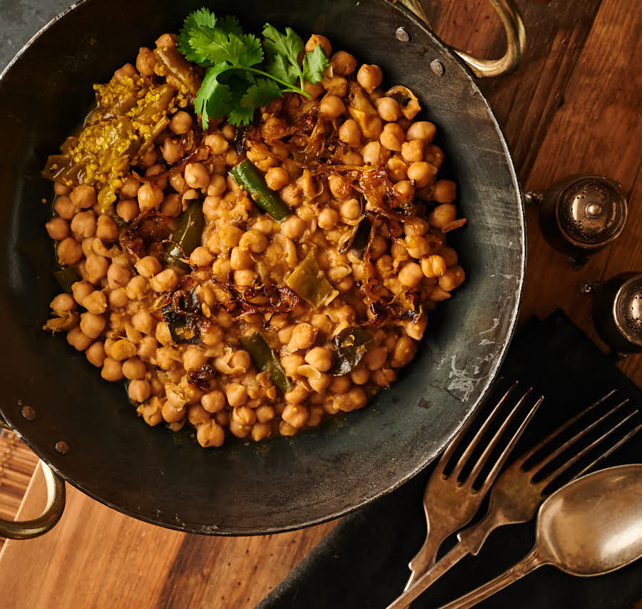 Green chili chana achari in a carbon steel bowl from above.