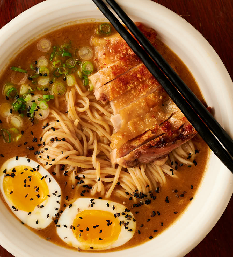 Closeup of bowl of curry chicken ramen garnished with black sesame seeds from above.