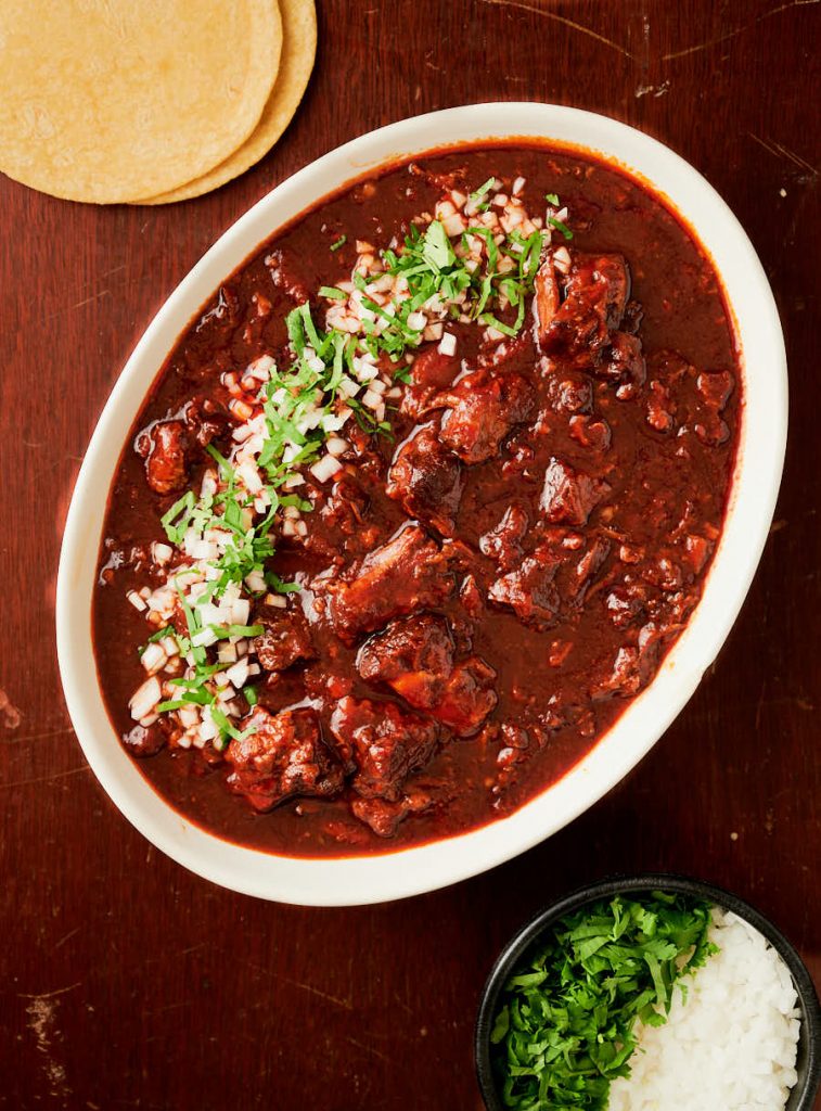 Big oval bowl of Birria garnished with onion and cilantro from above.