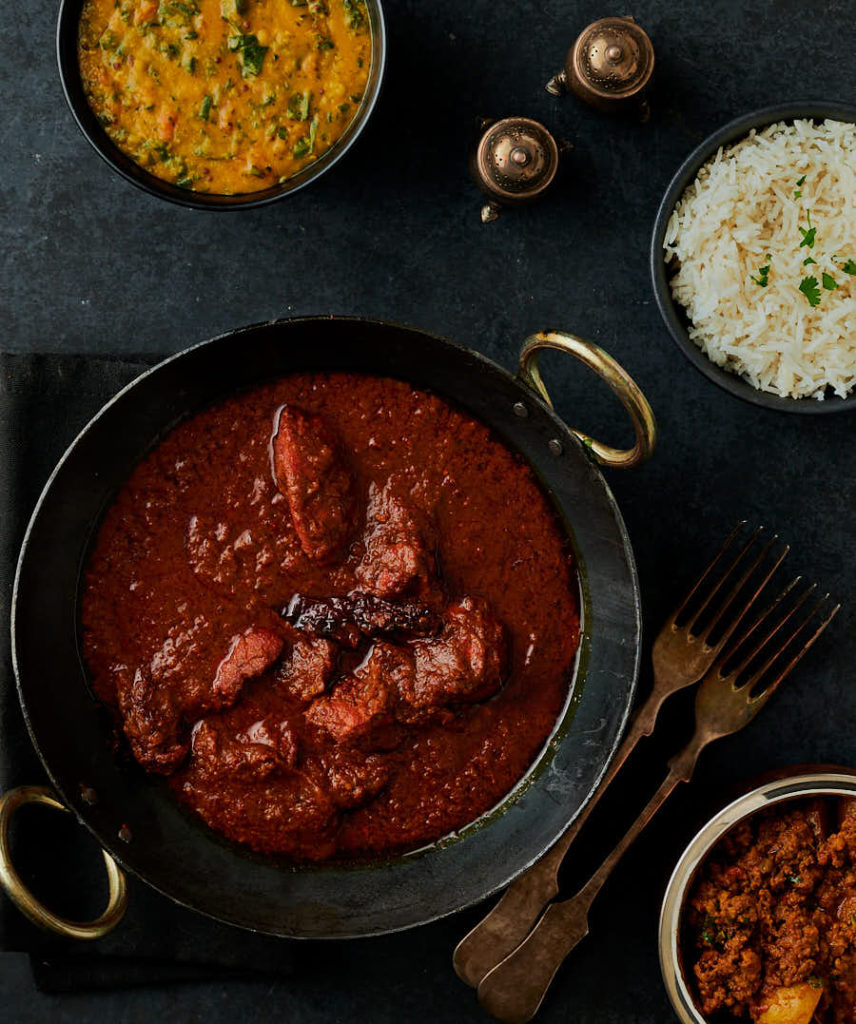 Table scene of chicken vindaloo with rice, dal and a keema curry from above.