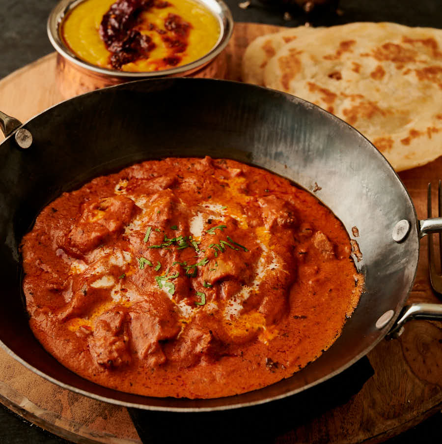 Hotel style butter chicken with parotha in a kadai from the front.