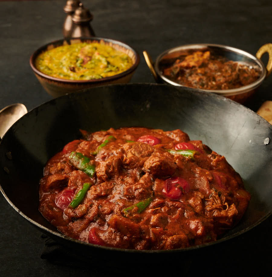 lamb bhuna in a kadai with tarka dal and chicken curry table scene from the front.