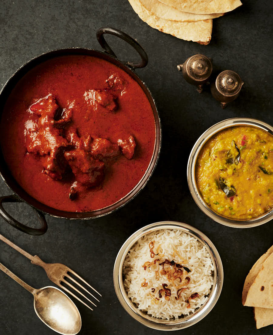 Table scene with chicken tikka masala, dal and rice.