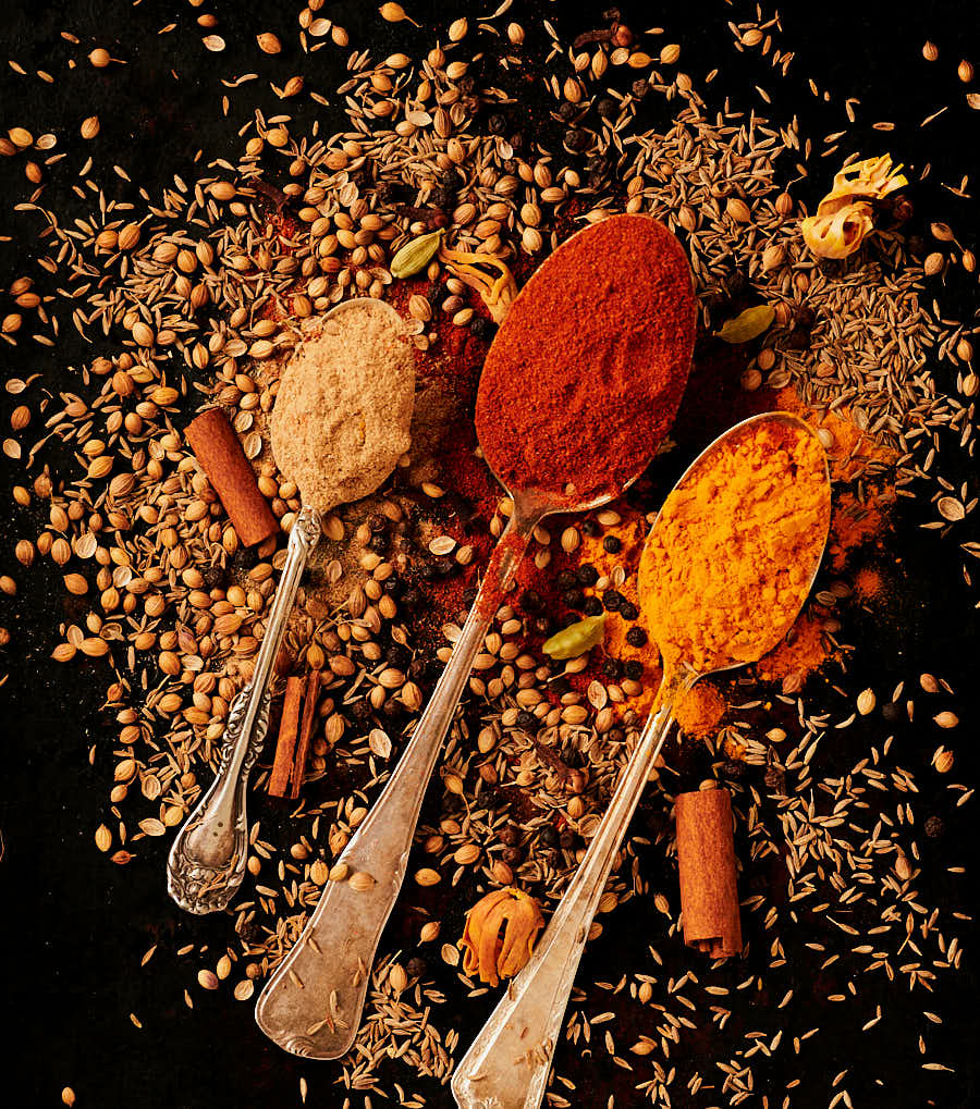 Spoons full of ground spices and scattered whole spices.