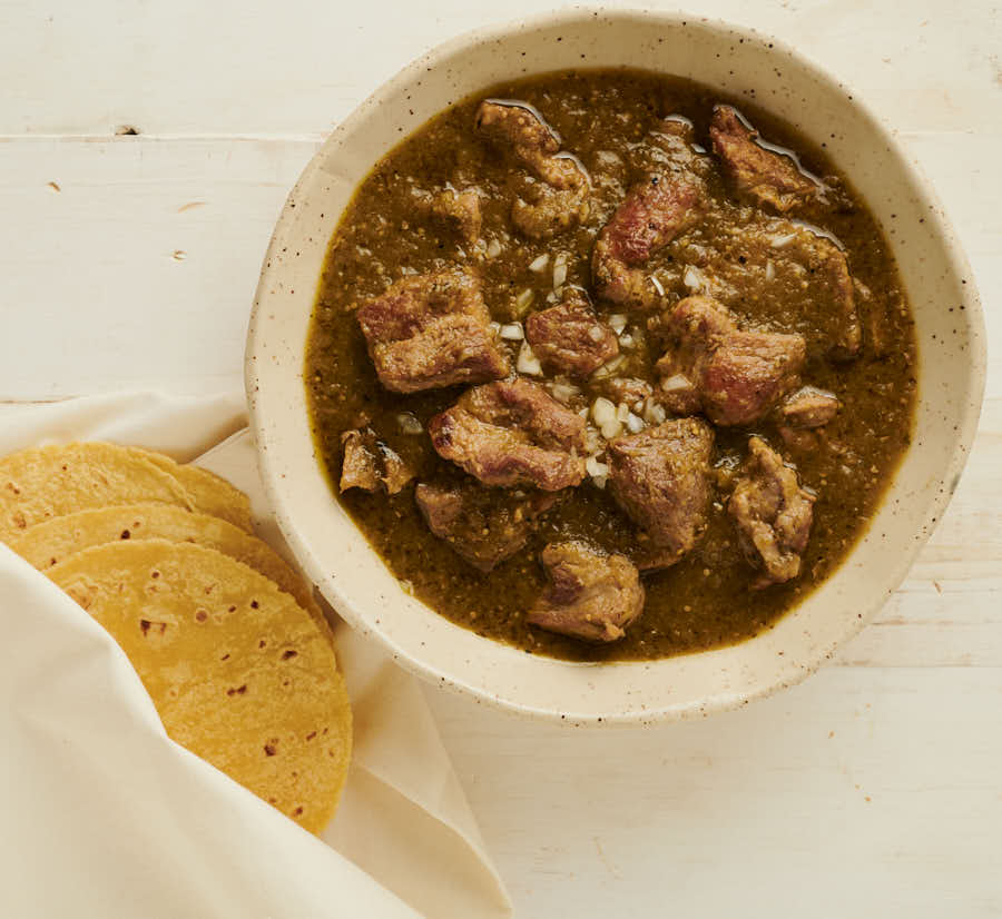 Bowl of chili verde and tortillas from above.