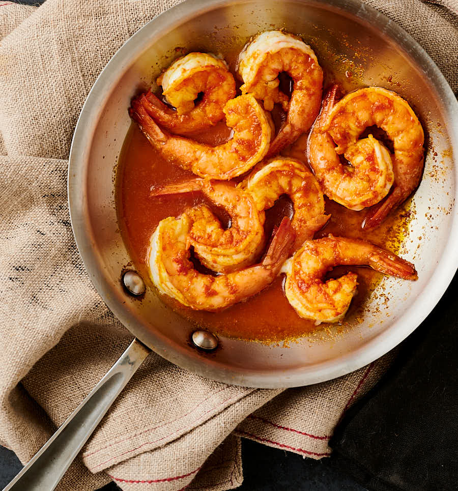 Barely cooked prawns in a small skillet from above.