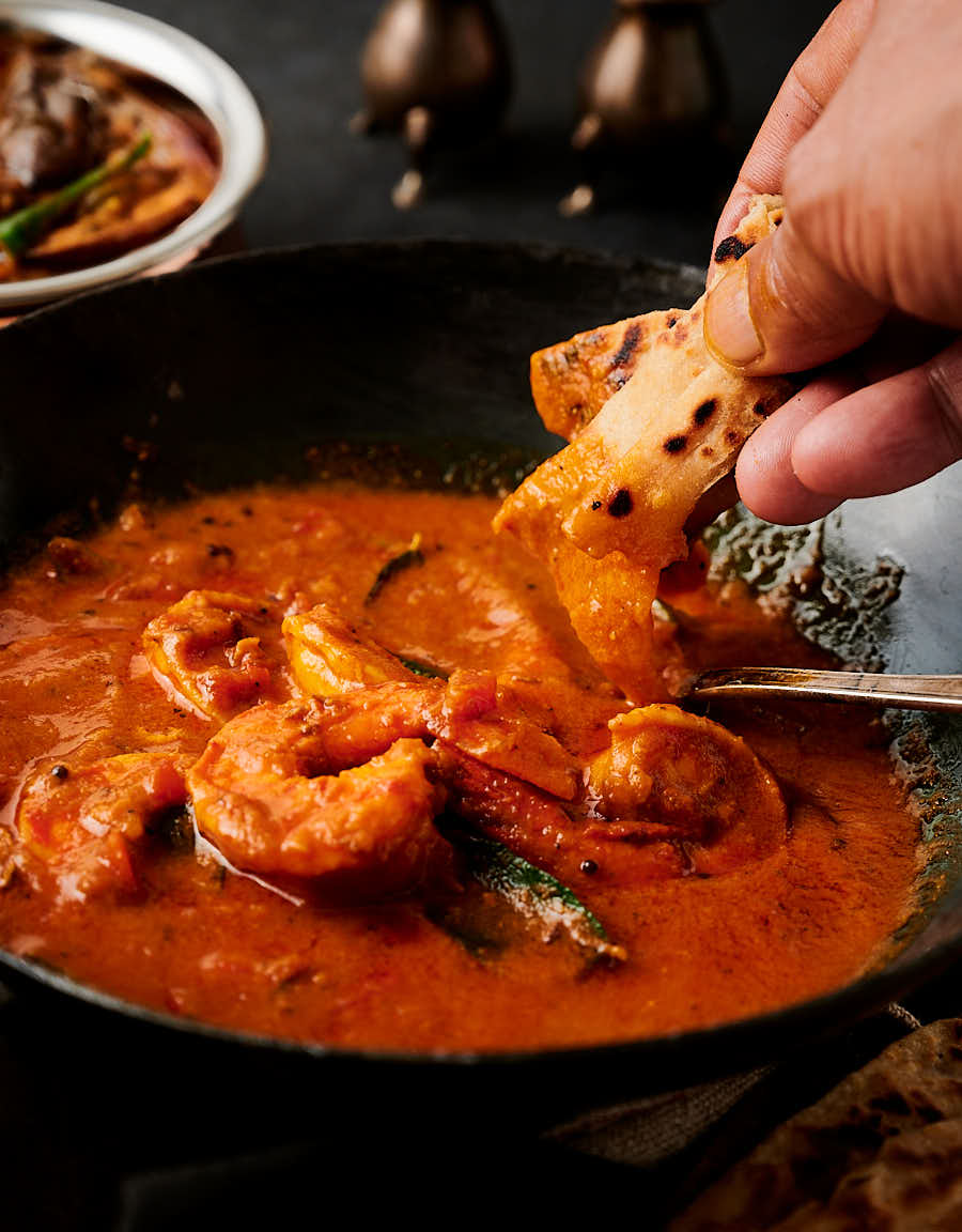 Dipping a piece of naan into prawn curry from the front.