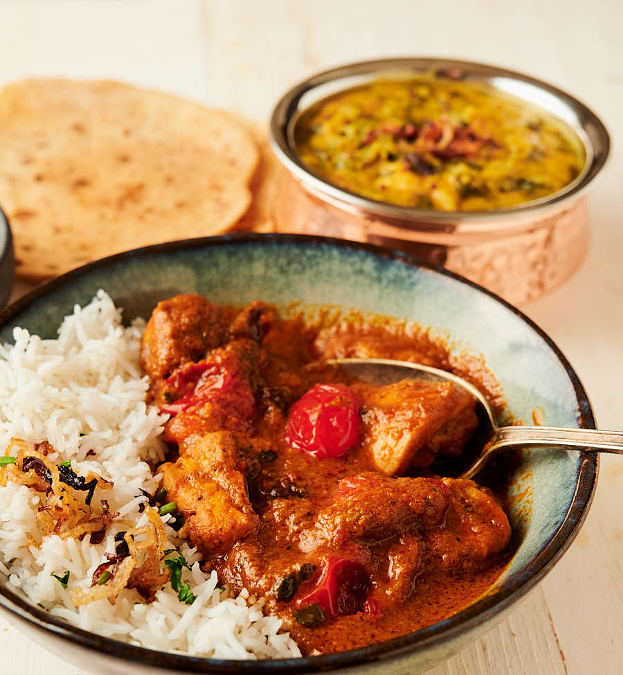 Bowl of chicken rogan josh with a spoon in it from the front.