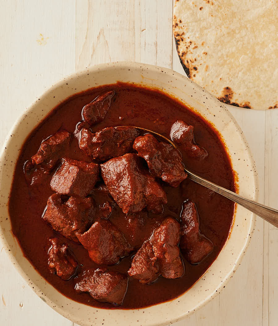 Carne adovada in a bowl with spoon and tortillas