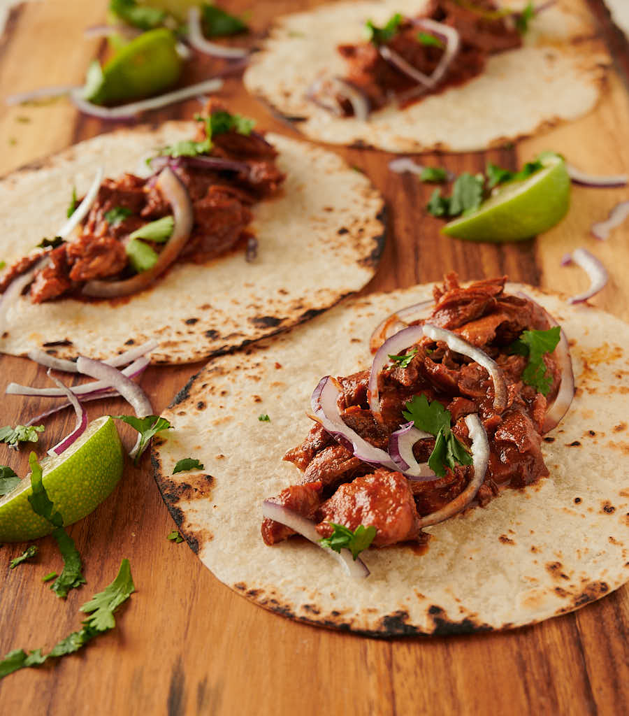 Tacos filled with carne adovada on a wood board from the front
