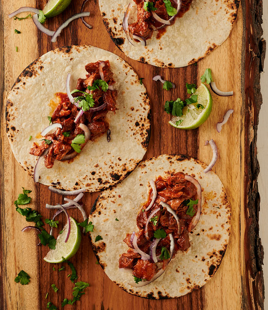 Tacos with carne adovada garnished with red onion.