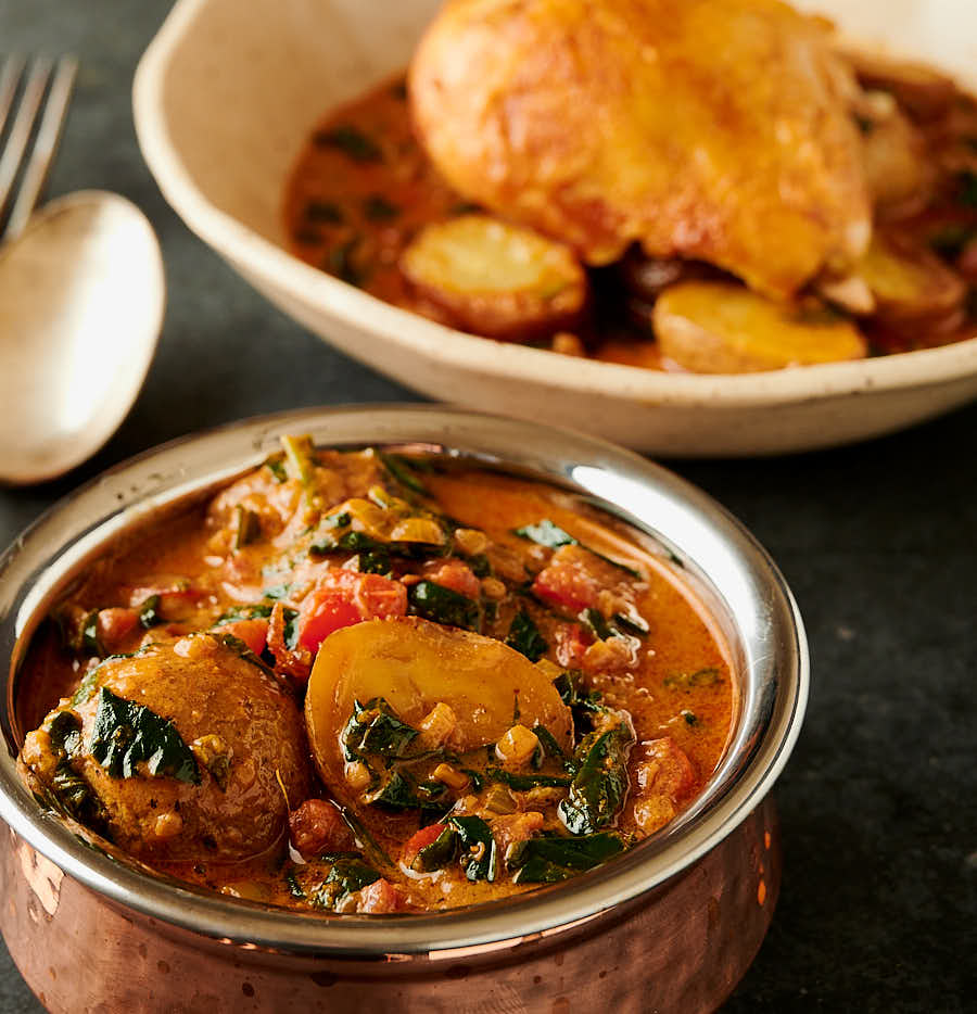 Bombay potatoes in a bowl from the front with plated Bombay chicken