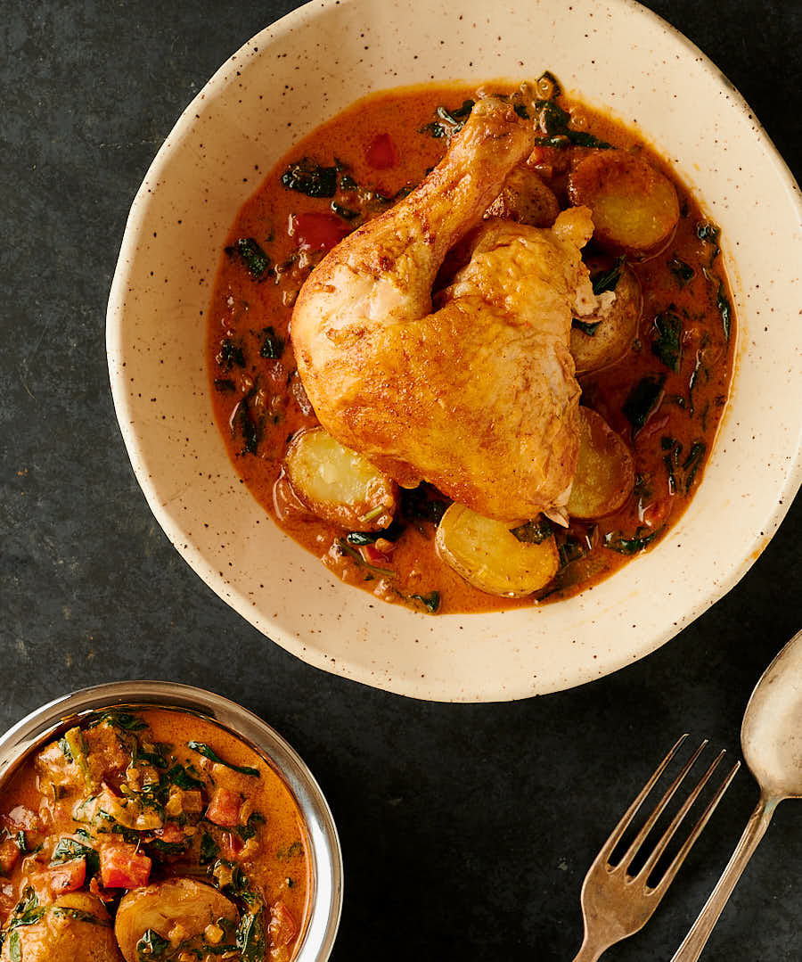 Bombay chicken leg in a serving bowl plated with potatoes and sauce from above