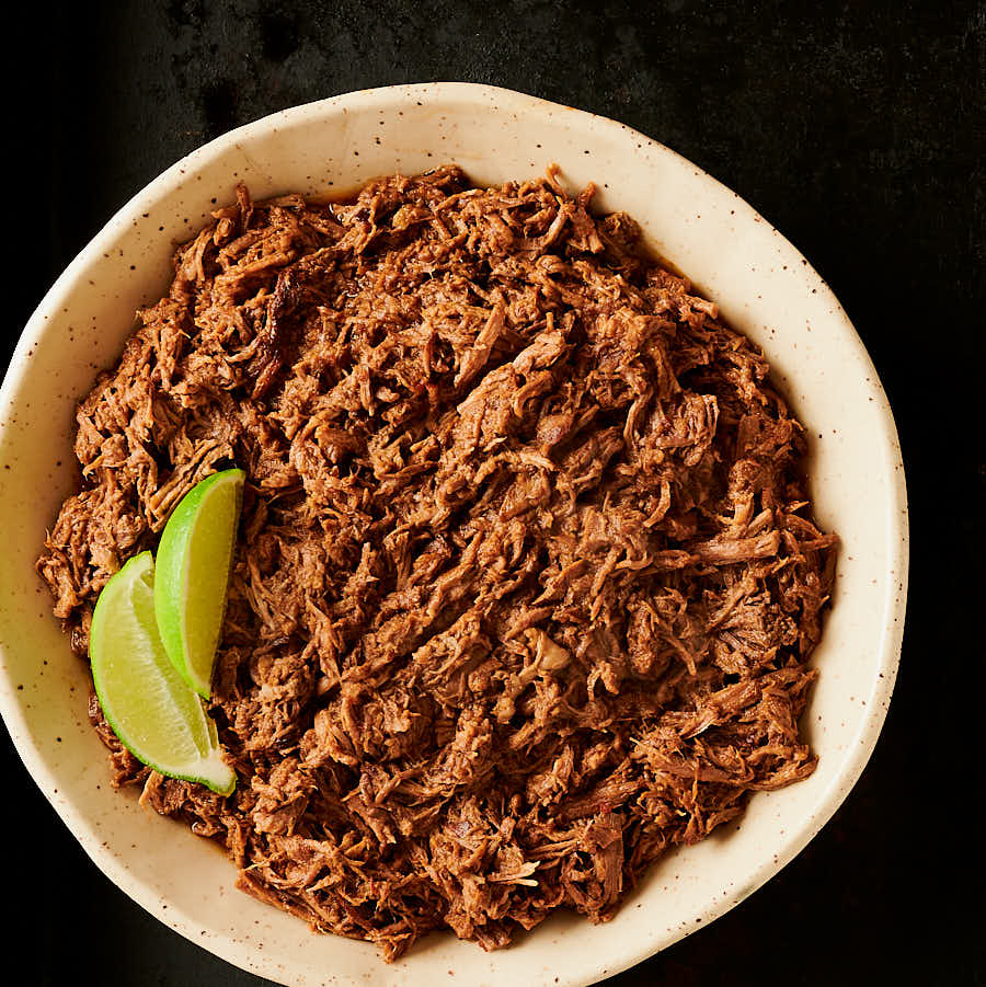 Beef barbacoa in a bowl garnished with lime from above.