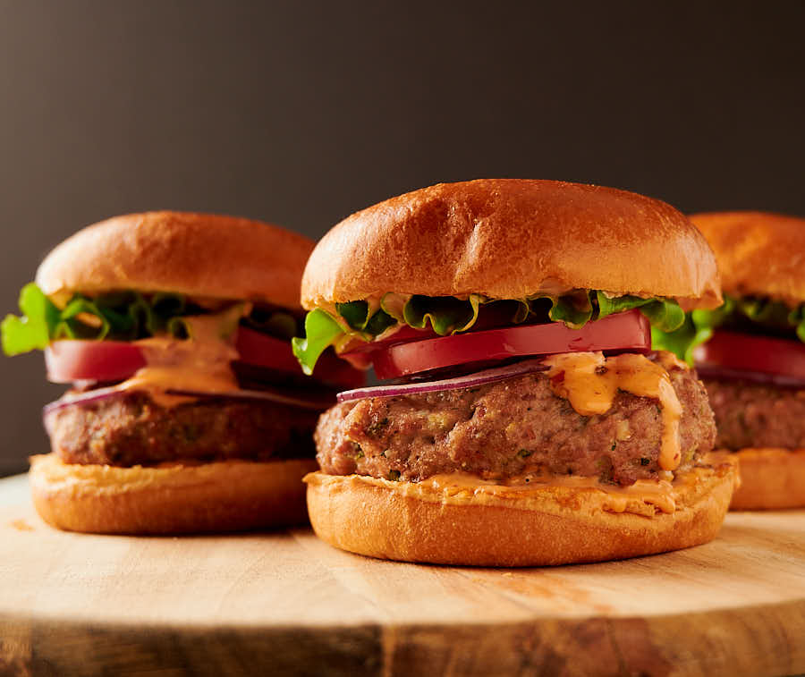 Three Thai turkey burgers on a cutting board from the front.