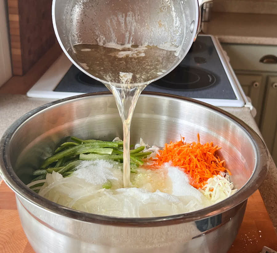 Pouring hot dressing mixture onto coleslaw vegetables from the front