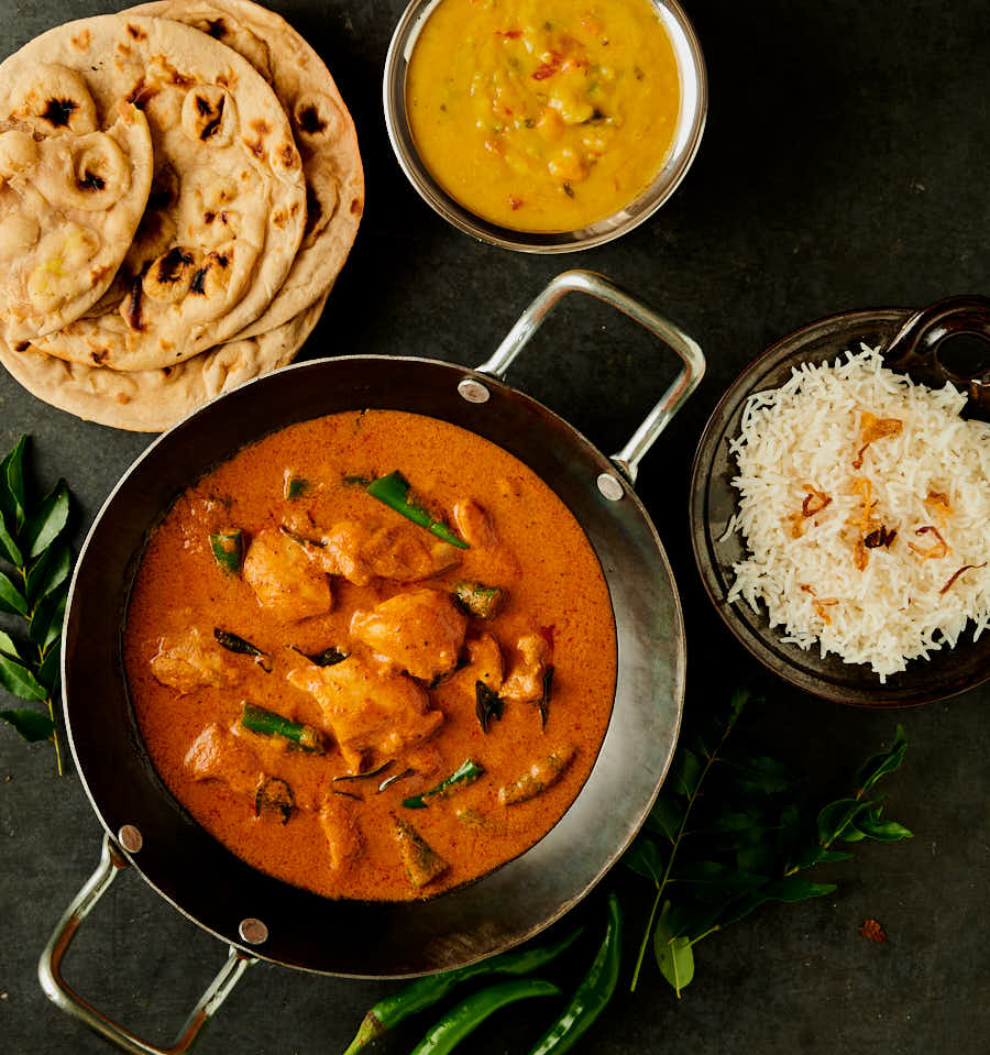Table scene with south Indian chicken curry, dal, rice and parathas