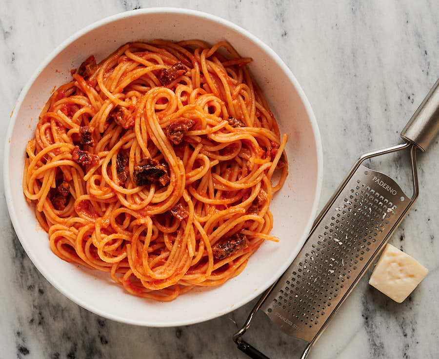 bowl of spaghetti all'amatriciana, pecorino romano and microplane cheese grater